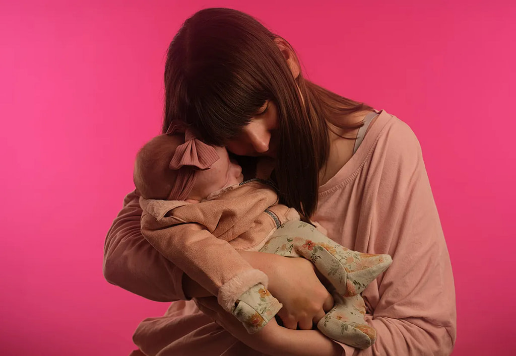 Intimate portrait of a mother holding her sleeping newborn baby, both with eyes closed against a vibrant hot pink studio backdrop, by Kaleid Studio