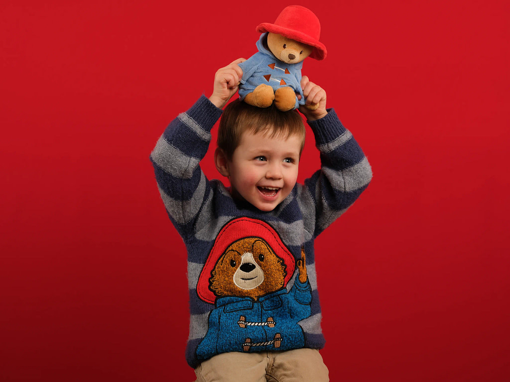 Studio portrait photography for teenagers. Boy, 14 in stripey black and red shirt spins a record on his finger in front of a colourful green background