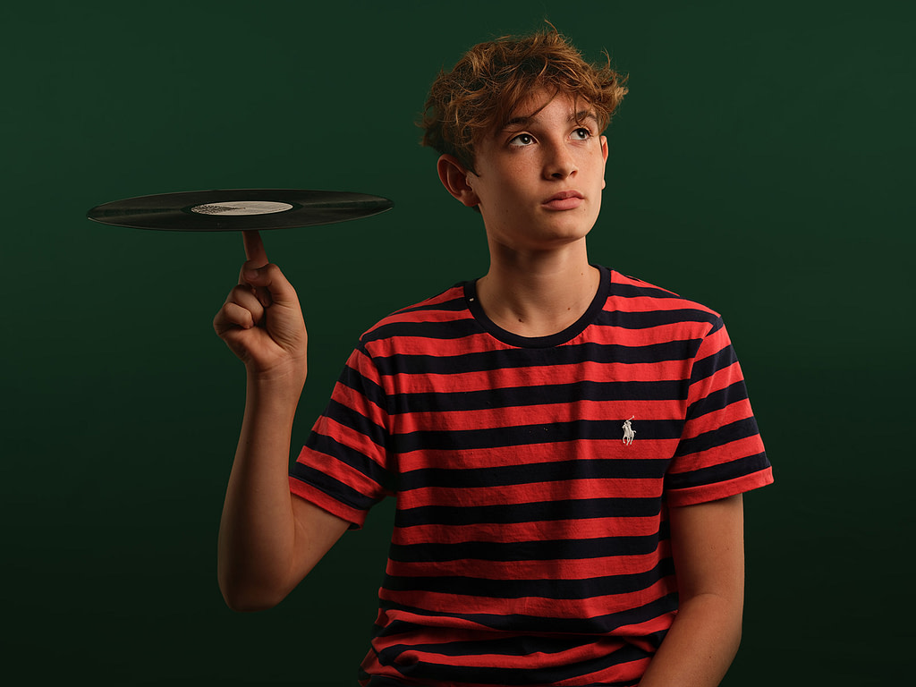 Stylised portrait of a teenage boy holding a vinyl record against a sage green studio backdrop, documenting personality and hobbies at Kaleid Studio.