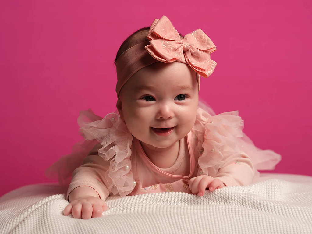 A professional studio-grade baby portrait on a vibrant pink background captured in a home session by Kaleid.