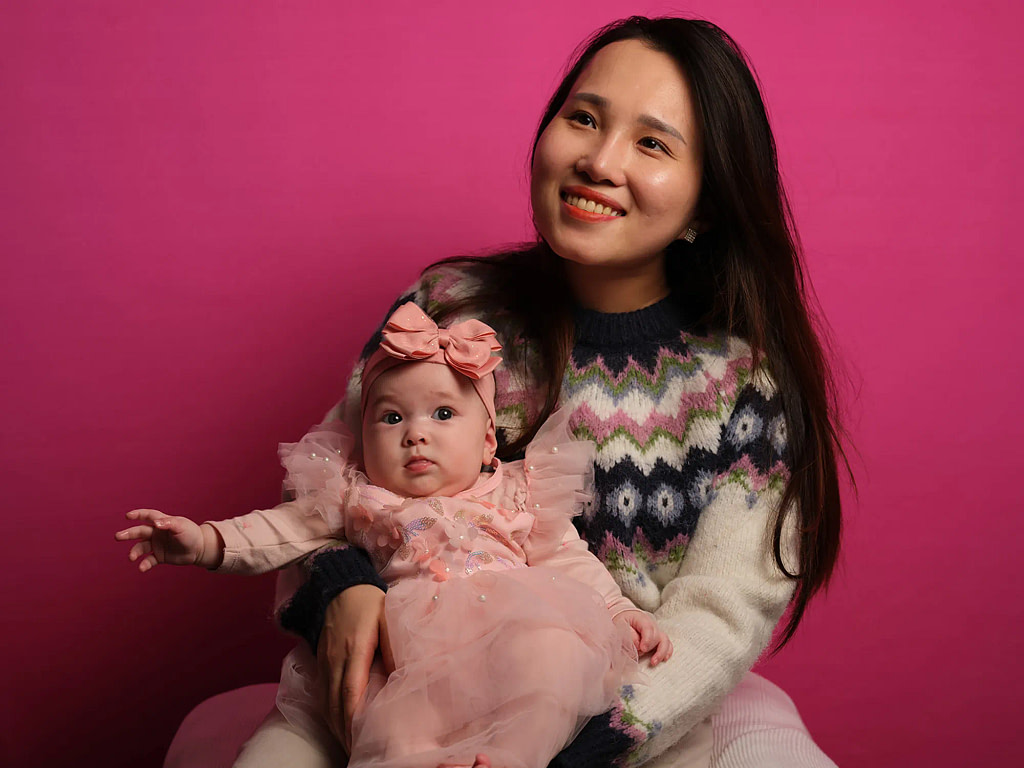 A professional mother and baby portrait captured in a home session by the Kaleid mobile studio, featuring studio-grade lighting on a vibrant pink backdrop.