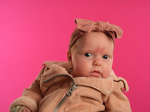 Detail-rich newborn girl portrait on a vibrant pink studio backdrop, capturing authentic baby character by Kaleid Studios